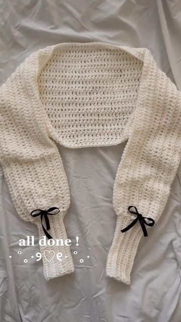 a white knitted sweater with black bows on the collar and sleeves, sitting on top of a bed