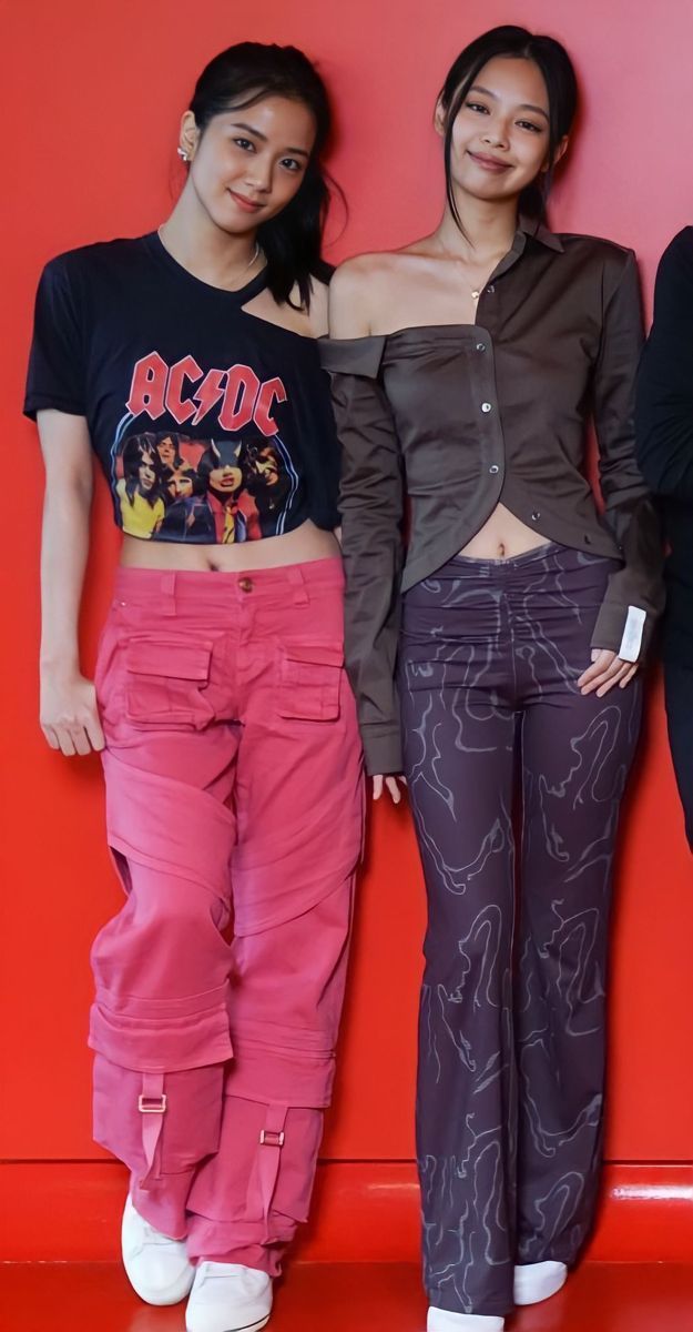 two women standing next to each other in front of a red wall with their hands on their hipss