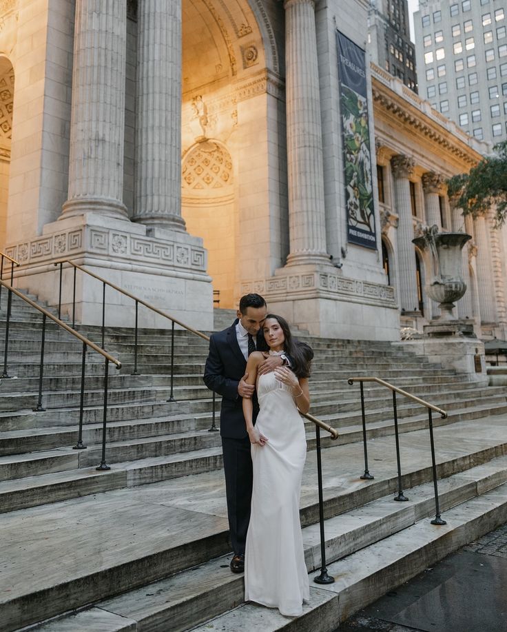 a bride and groom standing on steps in front of an old building at sunset with their arms around each other