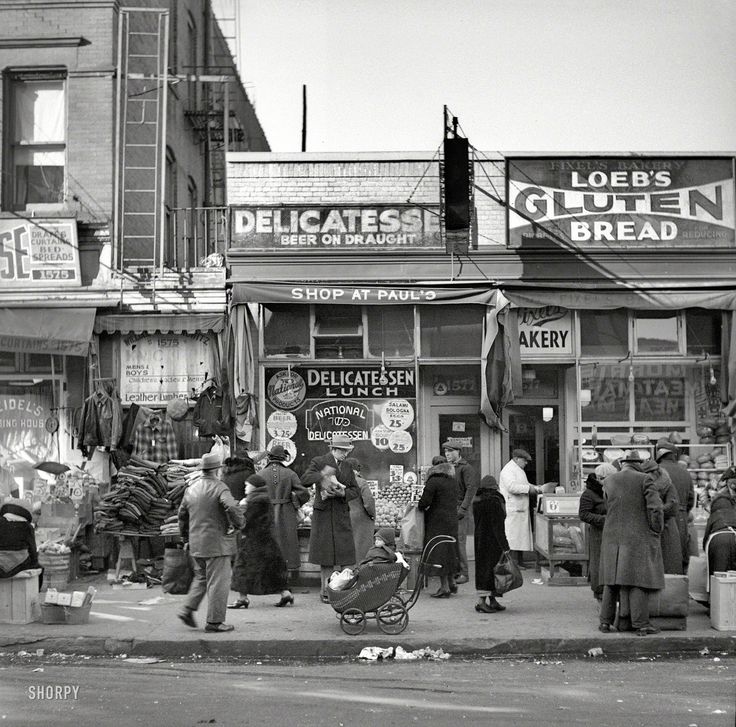 an old black and white photo of people on the sidewalk in front of a store