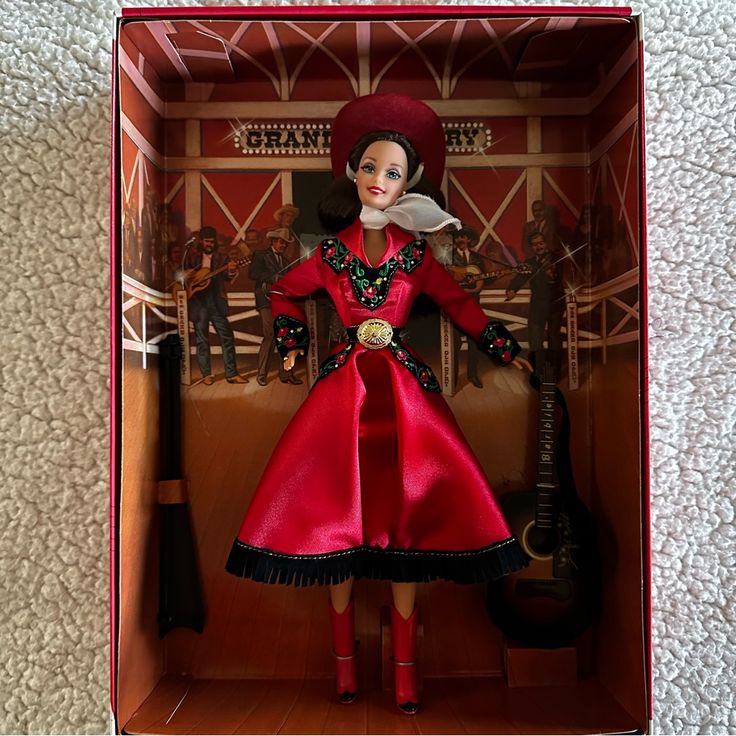 a doll in a red dress and hat inside a box on a white bed sheet