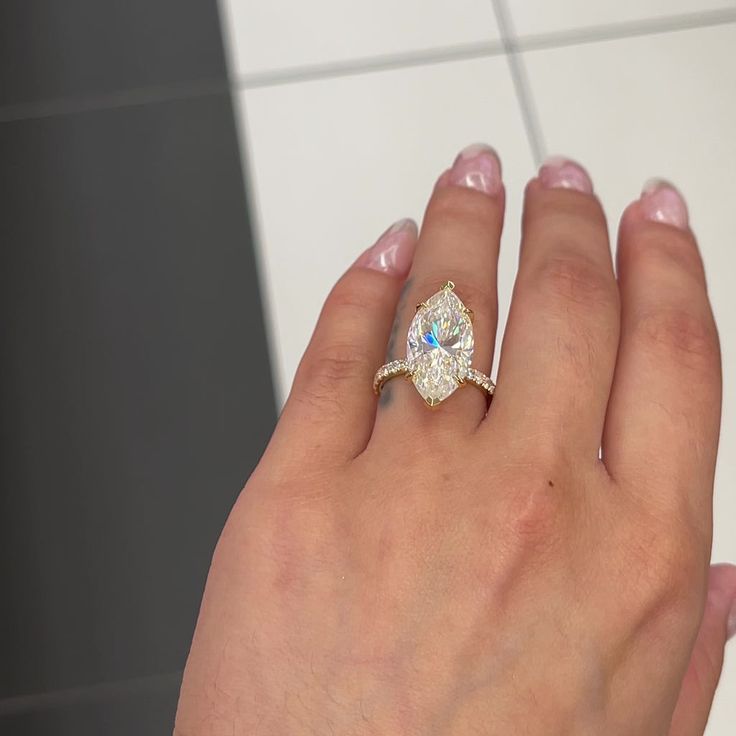 a woman's hand with a diamond ring on her left hand and a white tile wall in the background