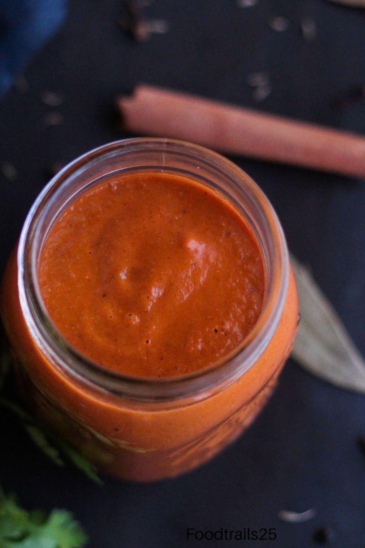 a jar filled with red sauce sitting on top of a table next to some vegetables