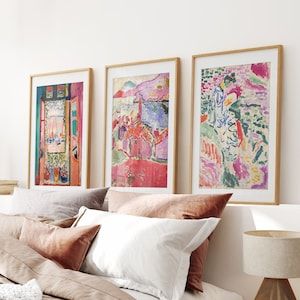 a bed with pillows and blankets on top of it next to two framed art pieces