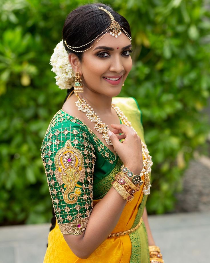 a woman in a green and yellow sari with flowers on her head, smiling at the camera