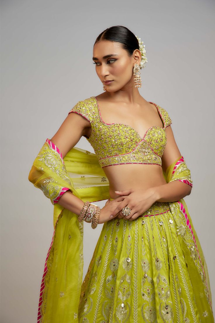 Editor's Note In a vibrant ensemble with exquisite marodi work and sequins, the billowing skirt is paired with a stunning neckline choli adorned with zardosi work. The soft organza dupatta with delicate motifs and borders adds a softer element—a story of love, passion, heritage, and beauty. Green Choli With Cutdana For Reception, Green Georgette Lehenga With Cutdana, Green Georgette Lehenga With Cutdana Details, Green Organza Dress With Cutdana, Green Organza Dress With Cutdana Detailing, Navratri Chandbali-shaped Tissue Silk Lehenga, Designer Green Choli With Sheer Dupatta, Green Chanderi Set For Reception, Fitted Green Lehenga With Cutdana