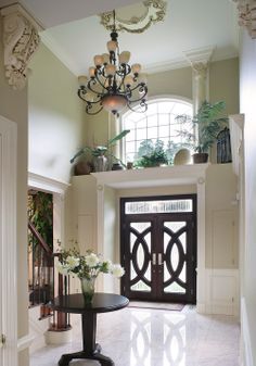 an entry way with a chandelier and flowers in the vase on the table