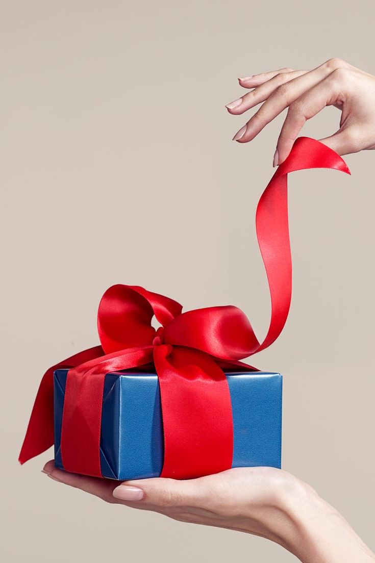 a person's hand holding a blue and red gift box with a red ribbon