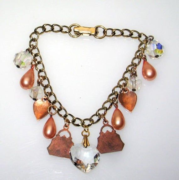 Antique Vintage Crystal Heart & Guilloche Red Enamel Charm Bracelet 7 3/8"Dainty gold finish link bracelet features 1920's - 1950's charms, which include: a large faceted crystal heart, 2 embossed copper purse / handbag shape charms with hand painted rose enamel hearts, 4 peach color faux pearl drops, 2 red guilloche enamel hearts, and 4 dangling Aurora Borealis crystal beads. Sweet and feminine!Don't miss this chance at a one-of-a-kind piece!UnmarkedMeasures approximately 7 3/8" long, 3/4" Vintage Jewelry With Adjustable Heart Charm, Vintage Adjustable Jewelry With Heart Charm, Vintage Jewelry With Heart Beads And Dangle Shape, Vintage Dangle Jewelry With Heart Beads, Vintage Dangle Heart Beads Jewelry, Vintage Heart-shaped Bracelets With Charm, Heart Shaped Vintage Bracelets With Vintage Charm, Vintage Charm Bracelet With Heart Charm, Vintage Heart-shaped Bracelet With Charm