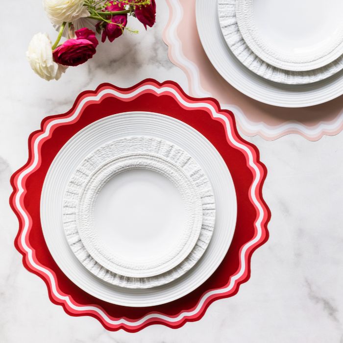 three white plates with red scalloped rims on a marble countertop next to a bouquet of flowers