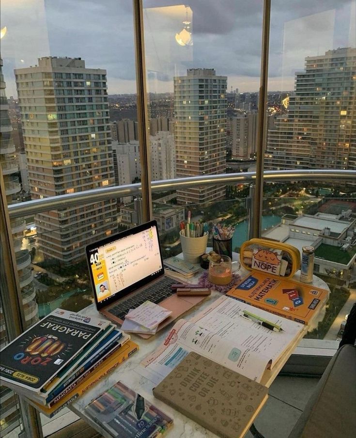 a laptop computer sitting on top of a desk next to a window filled with books