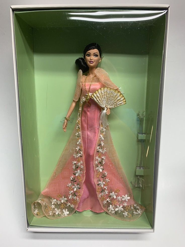 a barbie doll in a box holding a fan and wearing a pink dress with gold trim