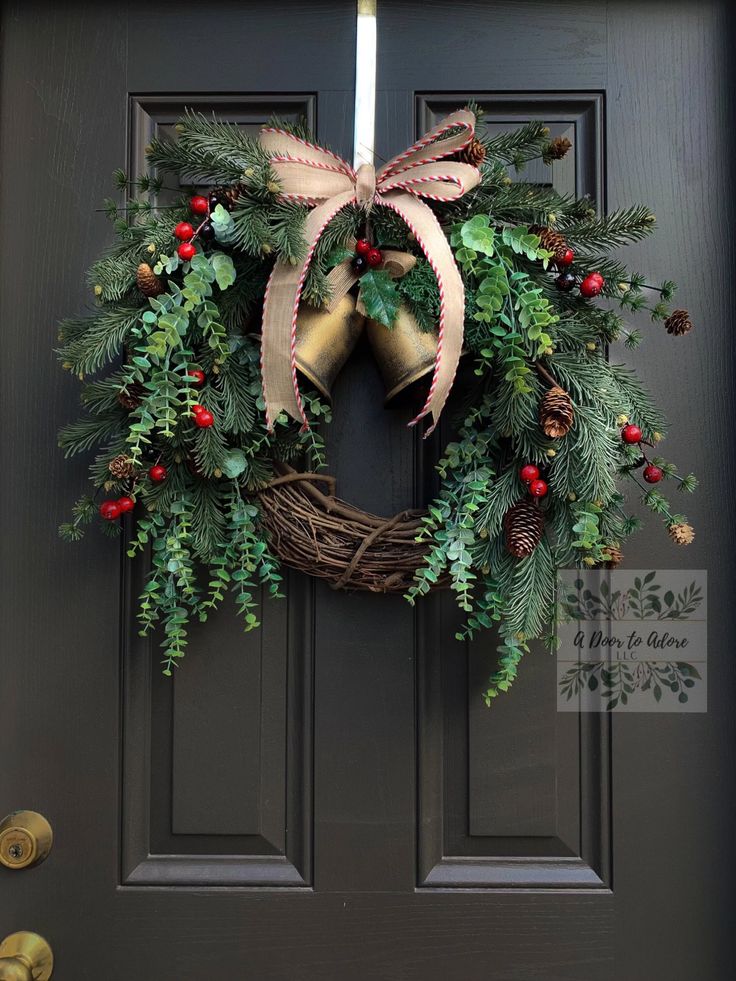 a christmas wreath on the front door with bells and greenery hanging from it's side