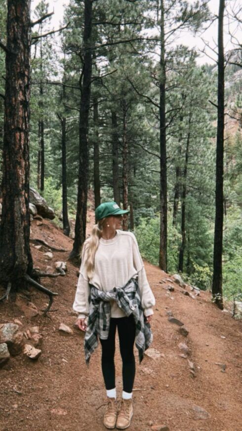 a woman walking down a dirt path in the woods wearing a green hat and scarf