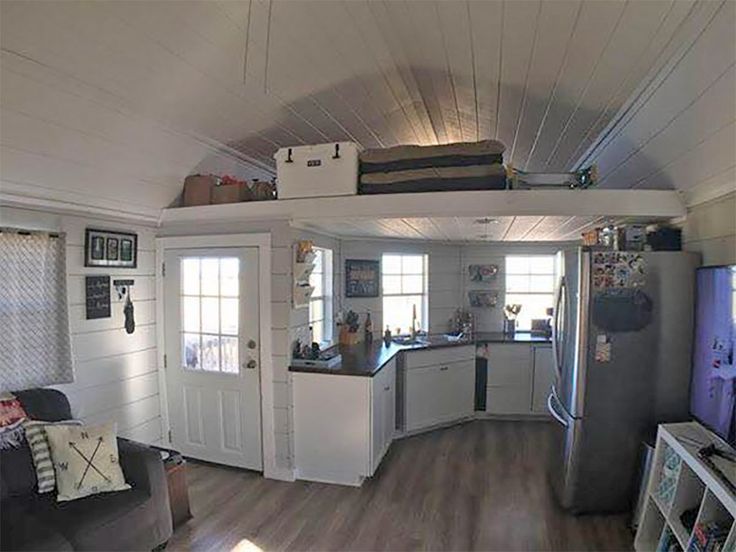 a living room and kitchen area in a tiny home with wood floors, white walls and ceilings