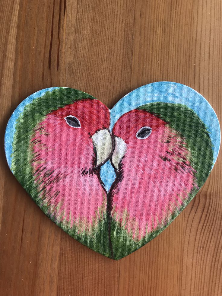 a painting of two pink parrots in a heart shaped frame on a wooden surface