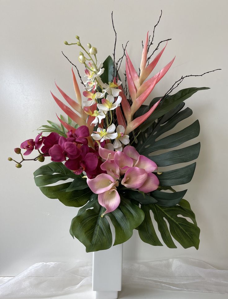 a white vase filled with lots of different colored flowers and greenery next to a wall