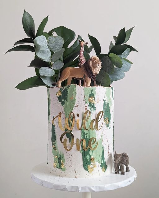 a cake decorated with greenery and figurines is on a white stand next to the wall