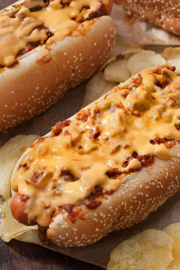 two hot dogs covered in cheese sitting on top of potato chips