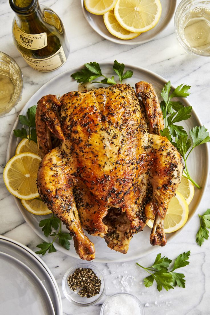 a whole chicken on a plate with lemons and parsley