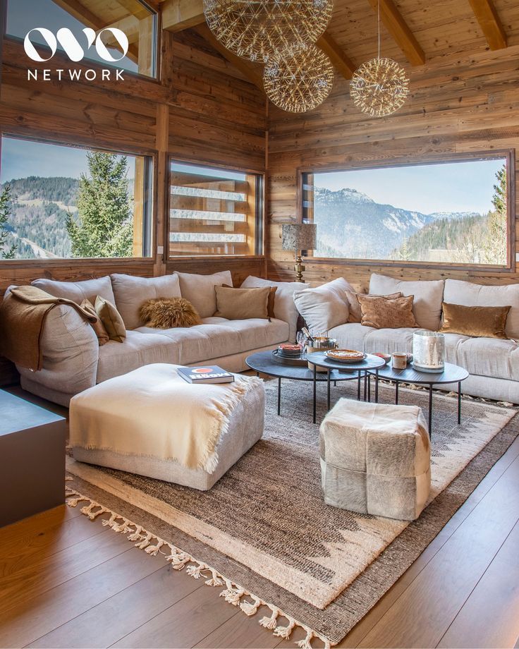 a living room filled with lots of furniture in front of large windows and wooden walls