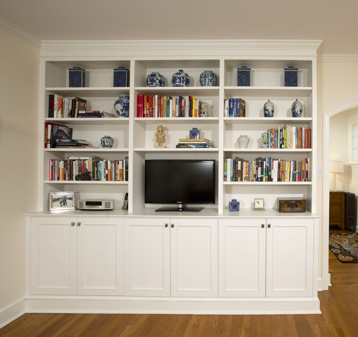 a living room filled with lots of white bookshelves next to a wooden floor