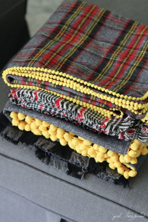 four blankets folded on top of each other in different colors and patterns, sitting on a gray couch