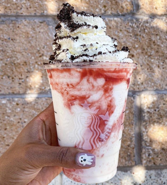 a hand holding up a drink with whipped cream and toppings