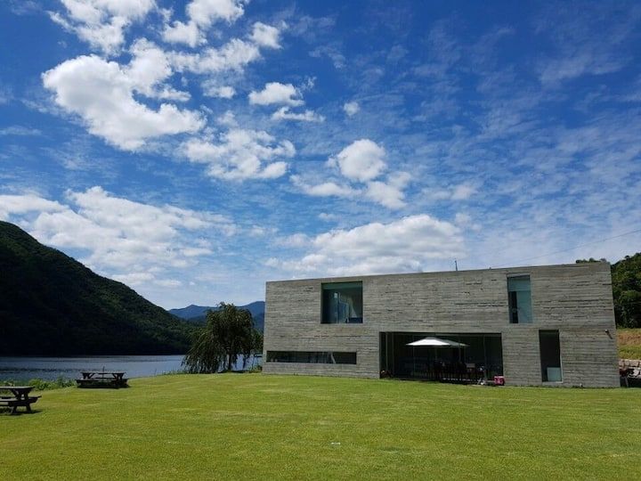 a house sitting on top of a lush green field next to a body of water