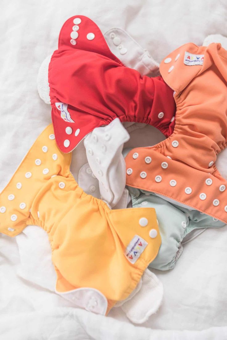 five cloth diapers laid out on top of a white sheet, all in different colors