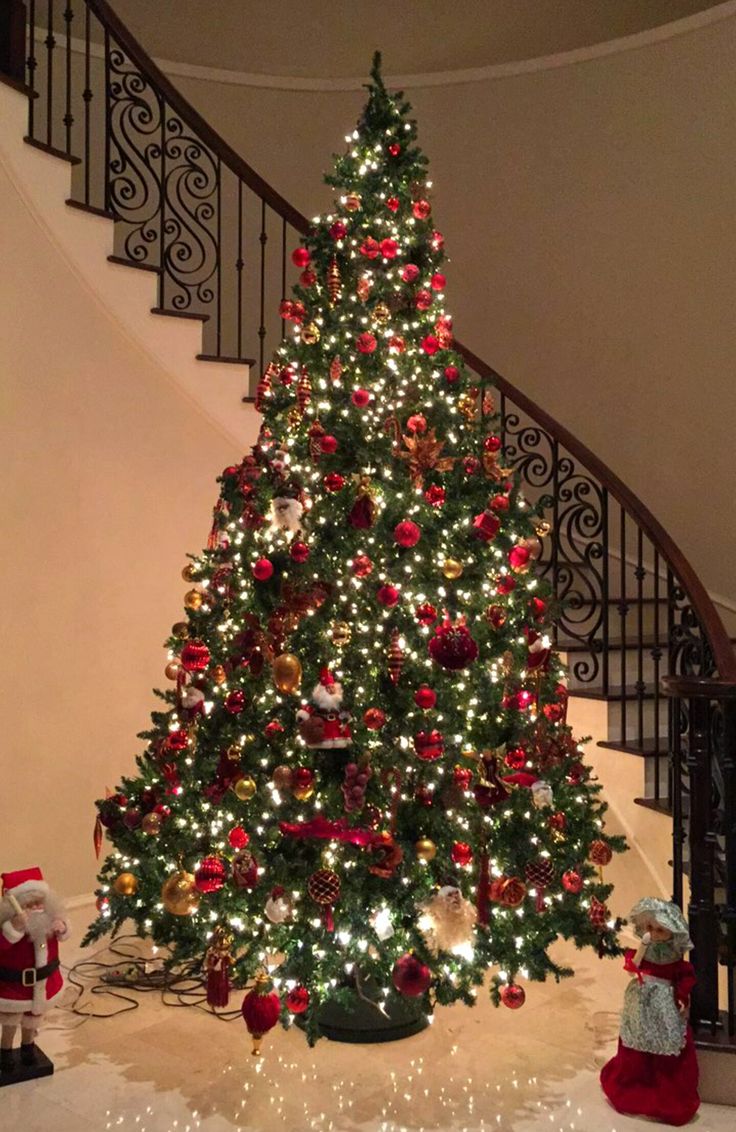 a decorated christmas tree sitting in the middle of a living room next to a stair case