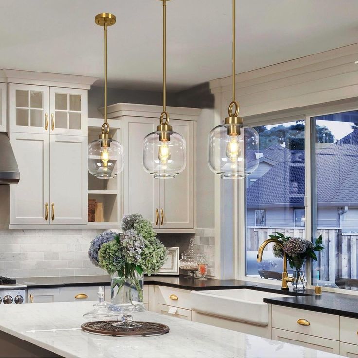 a kitchen with white cabinets and marble counter tops, gold pendant lights hanging over the island