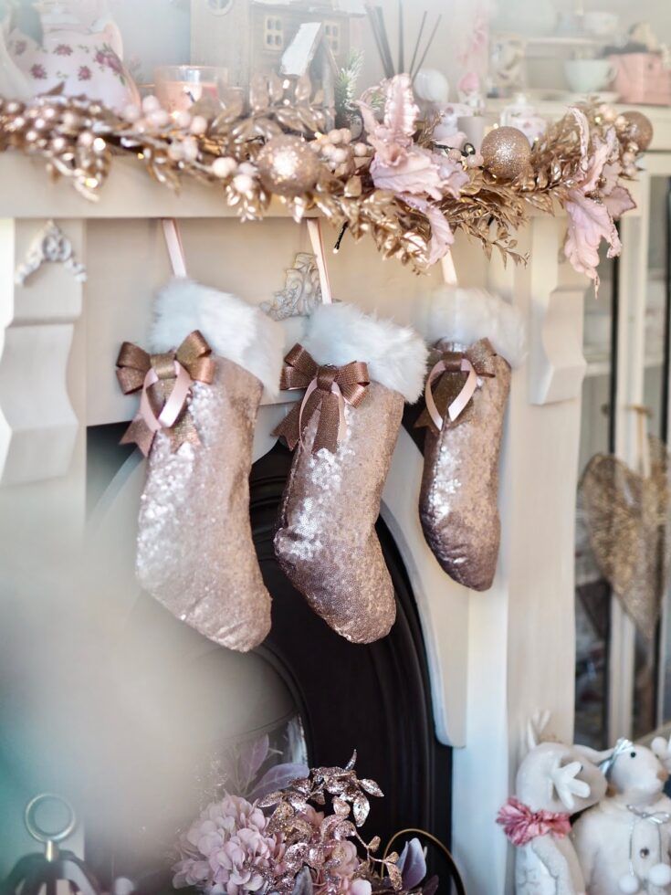 christmas stockings hanging from a mantel decorated with pink and gold decorations, along with other ornaments