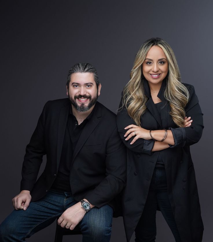 a man and woman posing for a photo in front of a dark background with their arms crossed