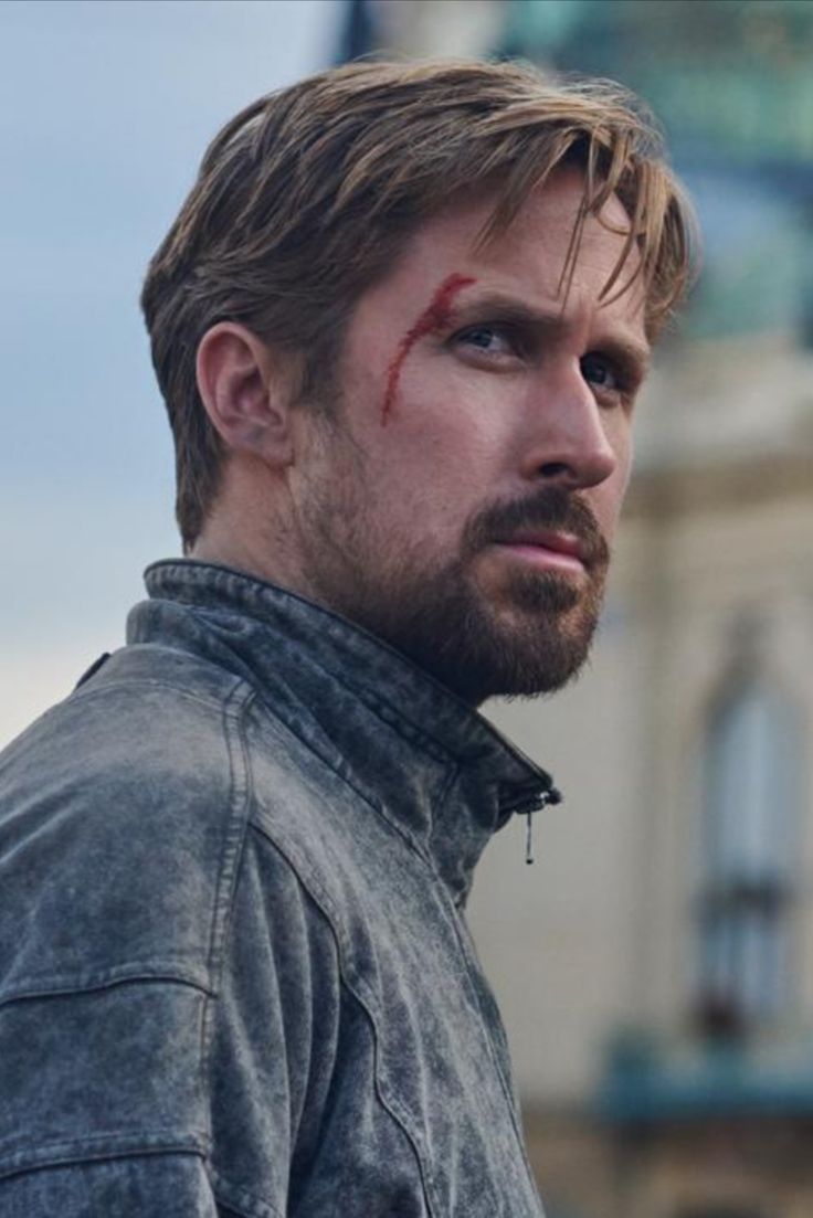 a man with blood on his face standing in front of a building and looking off to the side