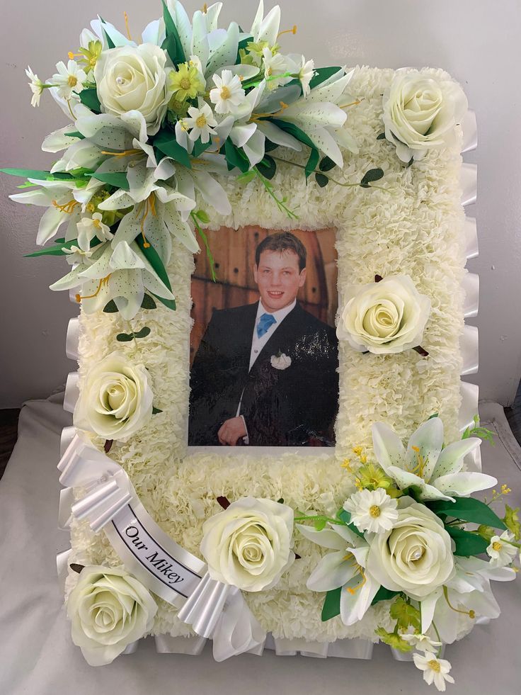 a photo frame made out of white flowers and greenery with a man in a tuxedo