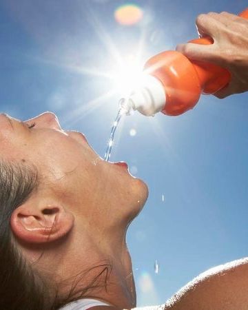 a woman drinking water from a bottle while standing in front of the sun with her eyes closed