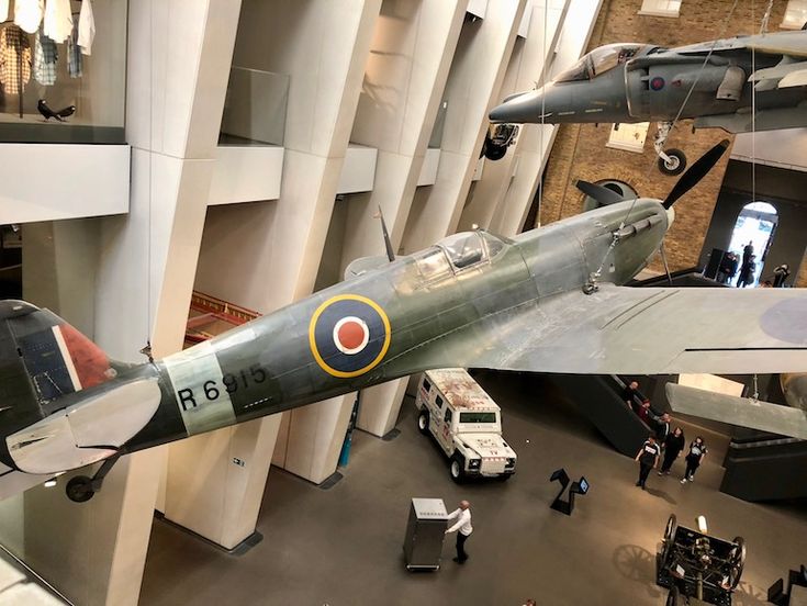 an airplane hanging from the ceiling in a museum with people looking at it and several other planes on display