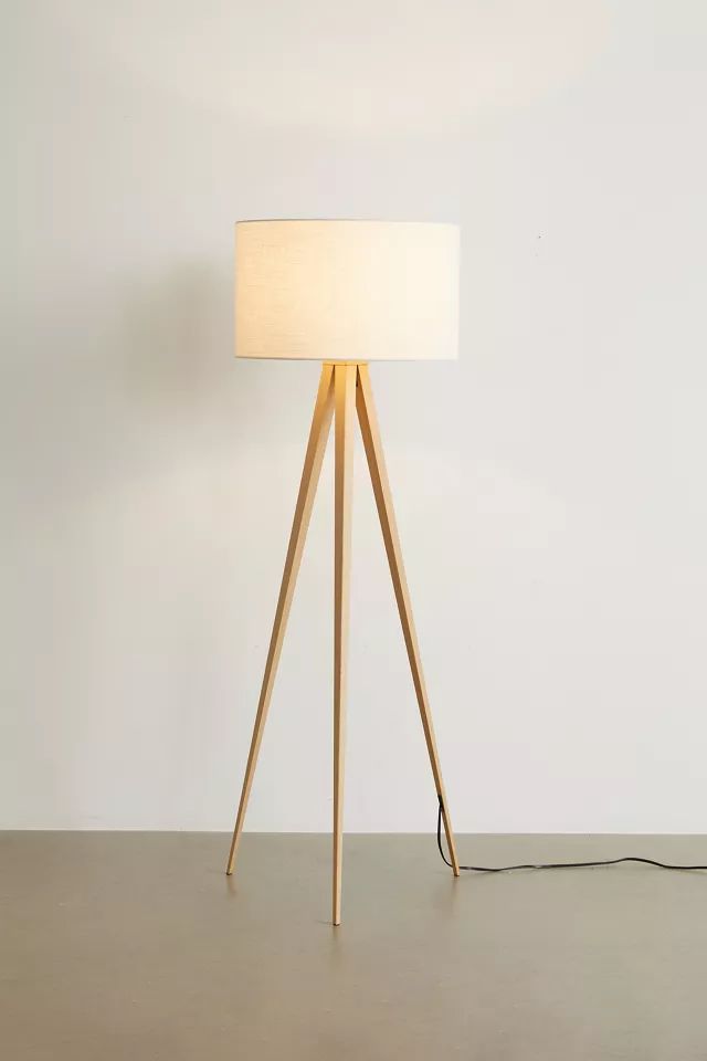 a wooden tripod floor lamp with a white shade on the top and a black cord plugged into it