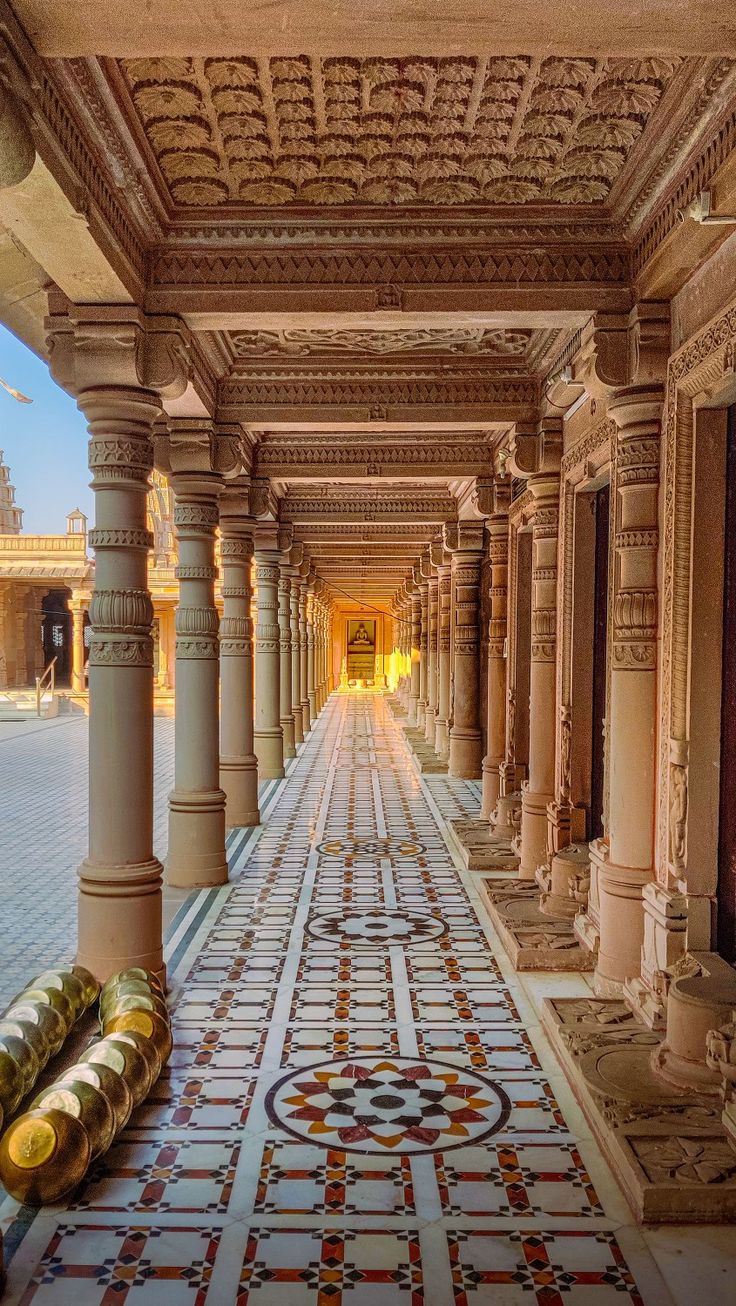 a long hallway with columns and tiled flooring in an old palace like setting, surrounded by ornately decorated pillars