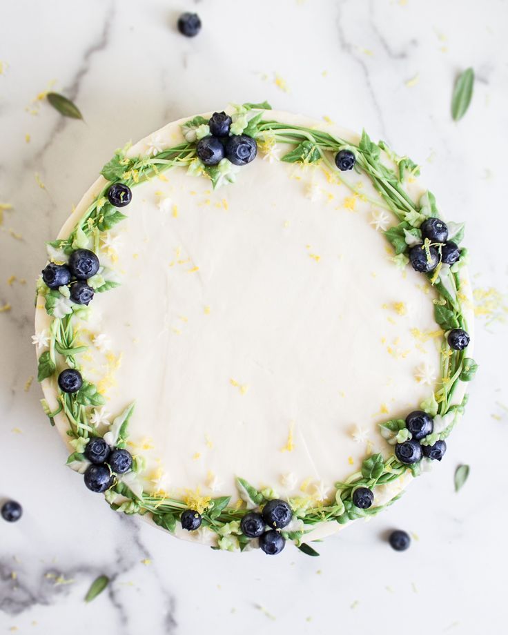 a cake decorated with blueberries and greenery on a marble counter top, surrounded by sprigs