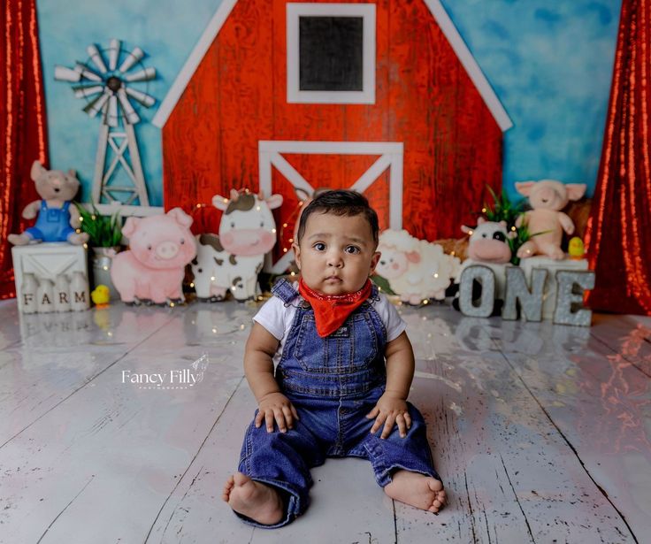 a baby sitting on the floor in front of a barn backdrop