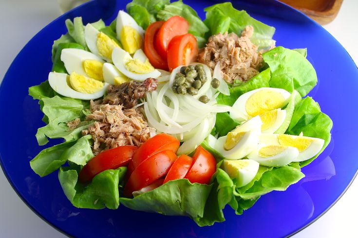 a blue plate topped with lettuce, tomatoes and hard boiled eggs