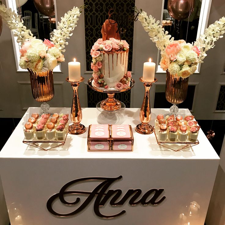 a table topped with lots of cakes and cupcakes next to tall vases filled with flowers