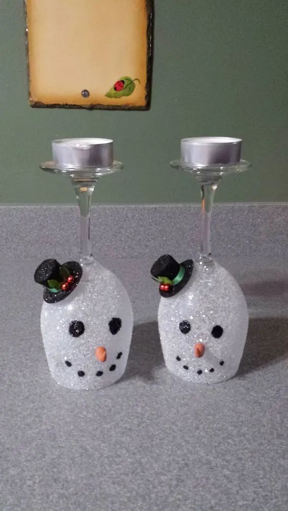 two wine glasses with snowmen on them sitting next to each other in front of a painting