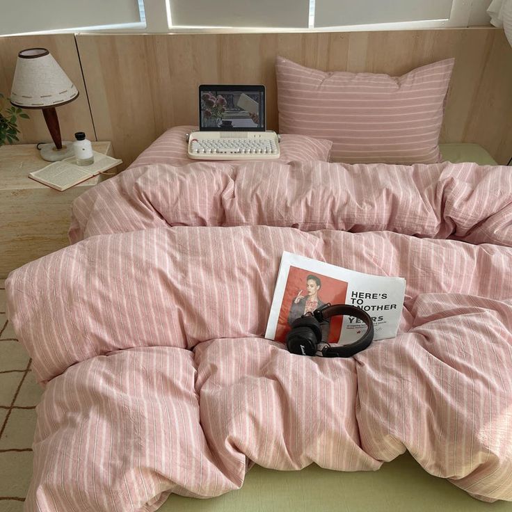 a bed with a pink comforter and pillows on top of it next to a laptop