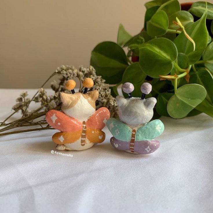 two small figurines sitting on top of a table next to plants and flowers