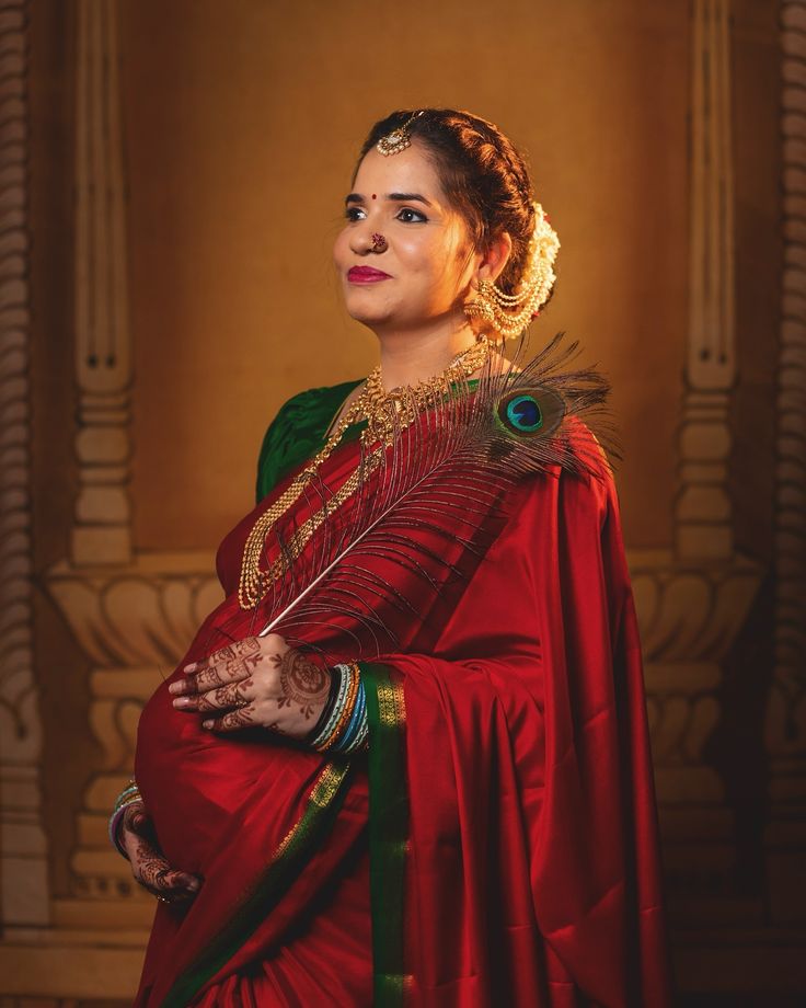 a woman in a red sari with a peacock feather on her shoulder, posing for the camera