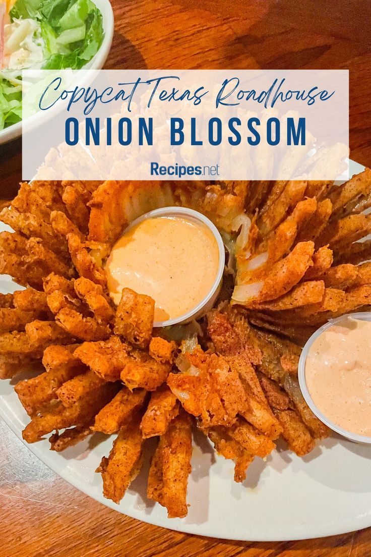 a white plate topped with onion blossoms and dipping sauce next to a bowl of salad