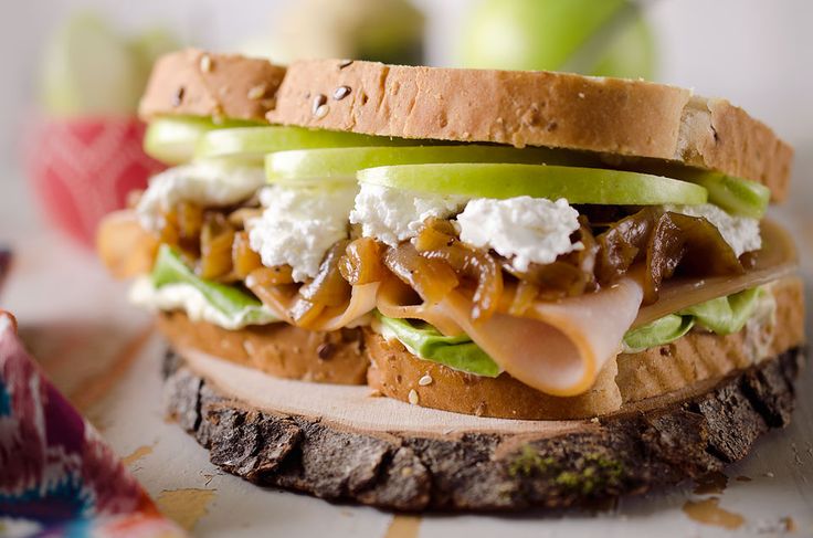 a close up of a sandwich with meat, cheese and apple slices on it sitting on a piece of wood